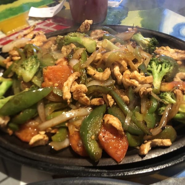 Sizzling chicken fajitas with broccoli, bell peppers, and onions on a hot skillet.