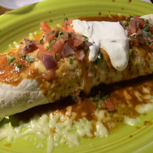 A Don Tequila Elyria burrito, topped with salsa, sour cream, and melted cheese on a green plate.
